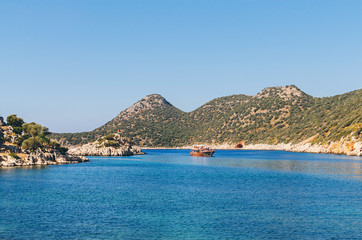 Fototapeta premium Panorama view of Tourist cruise near small rocky island in Ufakdere, Kas, Antalya, Mediterranean coast of Turkey