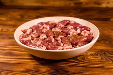 Ceramic plate with raw chicken hearts on wooden table