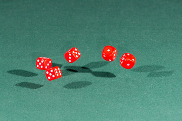 Five red dices falling on a green table