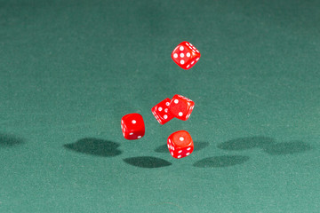 Five red dices falling on a green table