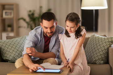 education and family concept - happy father and daughter with book and tablet computer doing homework together at home