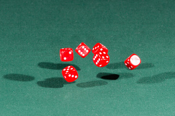 Six red dices falling on a green table