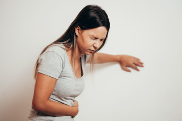 Portrait of young woman drunk or sick vomiting over gray background