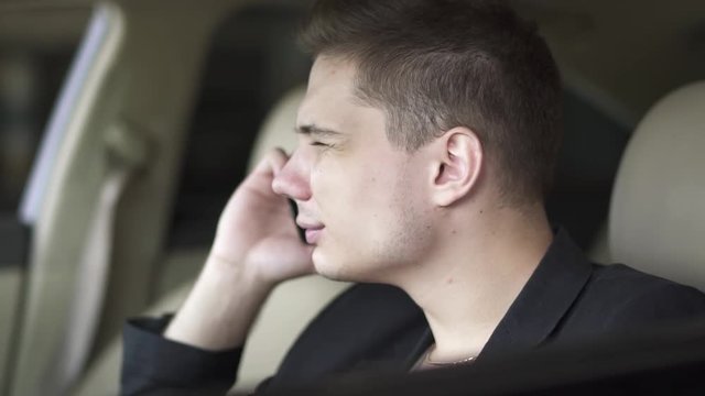 Portrait of young guy chewing gum and talking by cell phone in the car. Leisure of rich confident businessman.