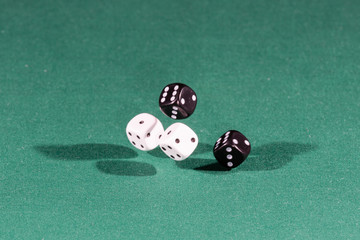 Four white and black dices falling on a green table