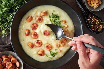 Flat lay of homemade cream of potato soup with croutons, fried vienna sausages and green coriander