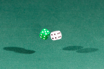 Two white and green dices falling on a green table