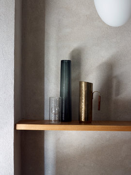 Glas Vasen und Messing Kanne auf Holzregal vor Steinwand in sch&ouml;nem Lichtspiel