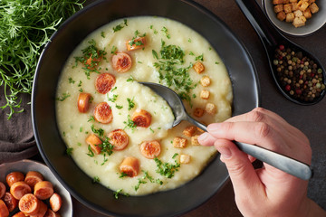 Flat lay of homemade cream of potato soup with croutons, fried vienna sausages and green coriander