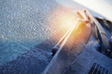 the wipers are covered with frost on the frozen glass of the car and the sun glare