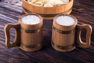 Two oak mugs with beer inside. On dark wooden background