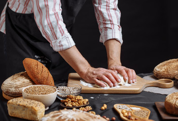 Male Chef kneads the dough with both hands until it becomes elastic, cooking delicious pizza or pastry over studio dark background.