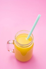 Colorful composition with mason jar glass full of fresh orange juice with straw, fruit, isolated on pink background. Close up, copy space, top view.