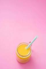 Colorful composition with mason jar glass full of fresh orange juice with straw, fruit, isolated on pink background. Close up, copy space, top view.