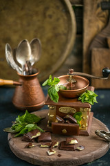 Coffee grinder and chocolate slices on a wooden board decorated with fresh mint. copy space for your text