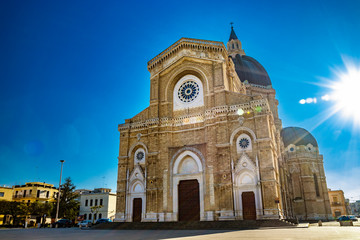 Fototapeta na wymiar Cathedral of St. Peter the Apostle, also known as Duomo Tonti, by Paolo Tonti. Facade, rose windows, portals, dome and apse. The blinding glare of the sun behind the building. Cerignola, Puglia, Italy
