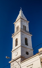 Fototapeta na wymiar Bell tower of the baroque church of the Beata Vergine del Monte Carmelo, Carmine church. White stone, mullioned window, sundial, bell, cross, arch. Cerignola, Puglia, Italy.