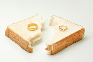 Two separate wedding rings with torn bread meaning to the word divorce.