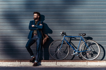 handsome bearded man in glasses and cap posing near bicycle