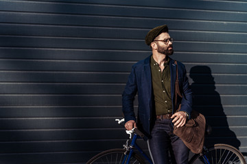 handsome bearded man in glasses and cap holding bicycle