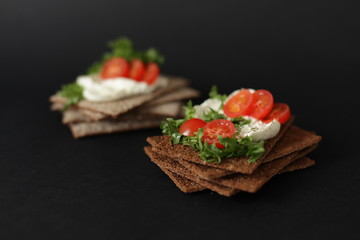 Healthy snack from wholegrain rye crispbread cracker with Cherry tomatoes, salad and soft cheese on black background