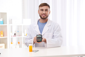 Pharmacist with payment terminal and pills in drug store