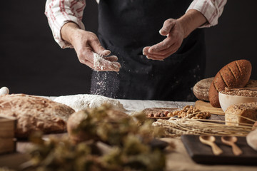 Unrecognizable male cook kneads dough as prepares delicious pastry, works at kitchen table with various bakery products and necessary for baking ingredients. People, healthy baking concept