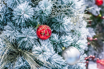 Fototapeta na wymiar Closeup decorated christmas branch with snow. Red ball bauble and other ornaments hang on the christmas branch tree with bokeh and colorful ribbons background. Merry christmas and happy new year.