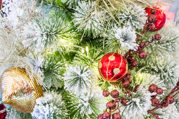 Closeup decorated christmas branch with snow. Red ball bauble and other ornaments hang on the christmas branch tree with bokeh and colorful ribbons background. Merry christmas and happy new year.