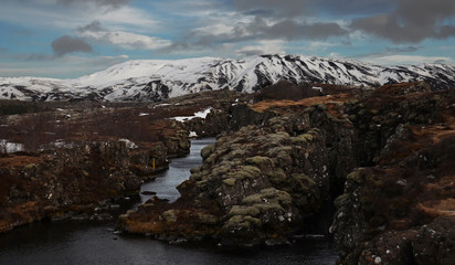 Typical Icelandic landscape: Thingvellir National Park, rivers, lava fields covered with snow against the backdrop of mountains and sky