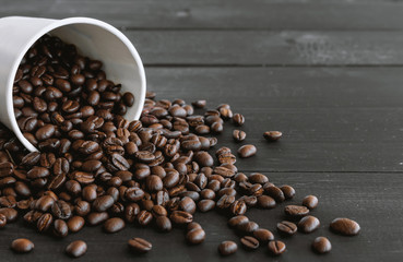 white paper cup and coffee beans on old wooden with soft-focus and over light in the background