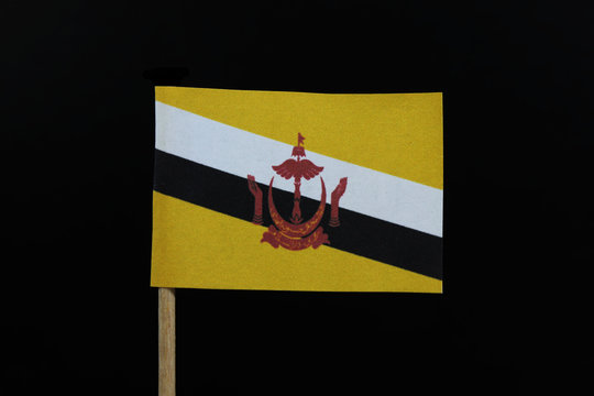 A official and unique  flag of Brunei on toothpick on black background. A centered red crest of Brunei on a yellow field cut by black and white diagonal stripes - Powered by Adobe