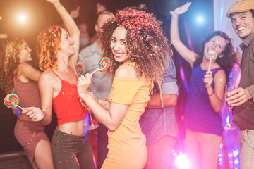 Happy friends dancing at vintage night party with confetti, champagne and candy lollipop