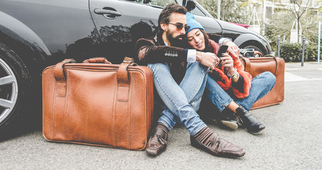 Fashion couple using smartphone app sitting outside of their convertible car