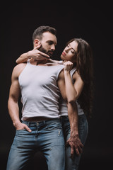 woman hugging and undressing man in white singlet isolated on black