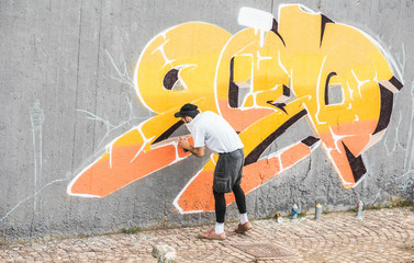 Graffiti artist covering his face while painting with color spray on the wall