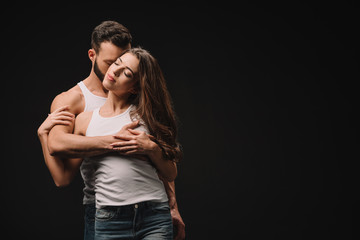 handsome man hugging and kissing young woman isolated on black