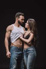 beautiful woman undressing man in singlet isolated on black