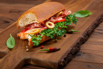 bitten off sandwich with vegetables, spices and ham decorated greens on dark cutting wooden desk