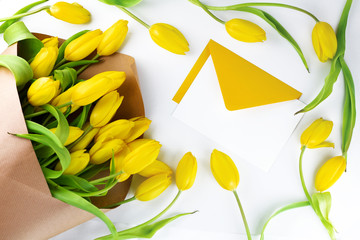 Composition with fresh yellow flowers, petals and open yellow envelope on white background. Flat lay, top view. Spring background, greeting card concept