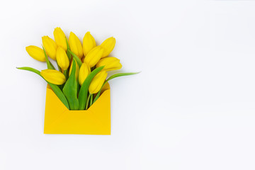 Fresh yellow spring flowers in envelope on white background, flower delivery concept, free space for text, greeting card with tulips