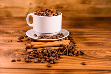 White cup filled with coffee beans, star anise and cinnamon sticks on wooden table