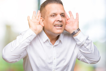 Naklejka premium Middle age arab elegant man over isolated background Trying to hear both hands on ear gesture, curious for gossip. Hearing problem, deaf