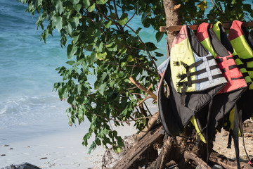 Colorful life jackets hanging on a rack on a tropical beach with copy space. Equipment for active...