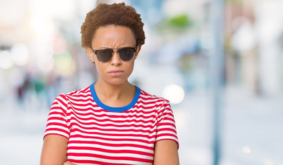 Beautiful young african american woman wearing sunglasses over isolated background skeptic and nervous, disapproving expression on face with crossed arms. Negative person.