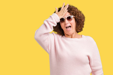 Beautiful middle ager senior woman wearing pink sweater and sunglasses over isolated background...