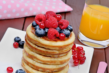 Pancakes in a plate with fresh berries and orange juice on wooden table