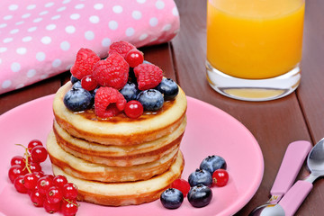 Delicious pancakes with fresh berries in a pink plate and orange juice