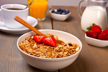 A plate with muesli, strawberries, juice, honey and milk on a white background.