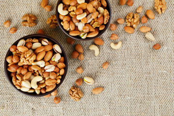 Mix of various nuts in a wooden cup against the background of fabric from burlap. Nuts as structure and background, macro. Top view.